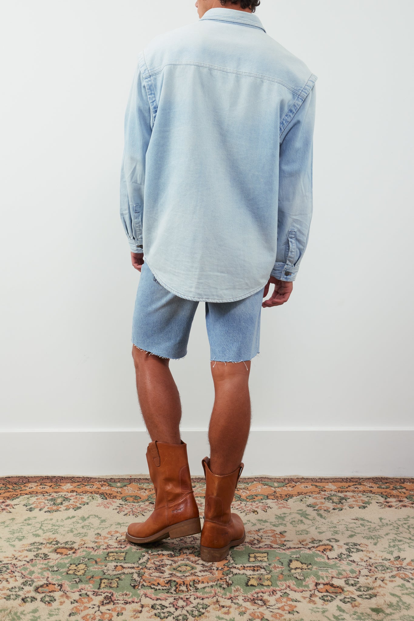 Person wearing a light blue shirt, shorts, and brown boots on a patterned rug.