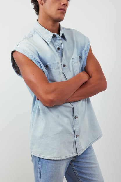 Man wearing a light blue sleeveless denim shirt against a white background
