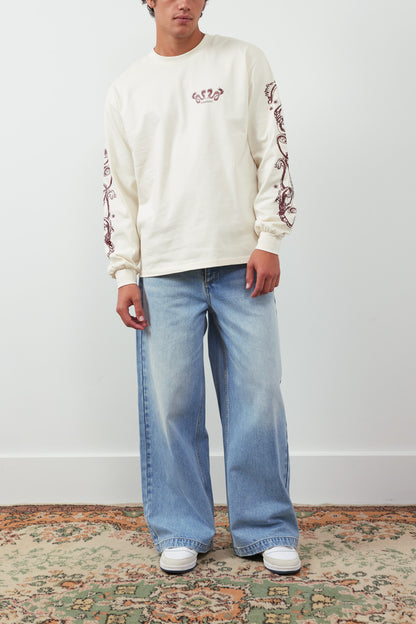 Person wearing a cream sweatshirt with floral patterns and light blue jeans on a plain background