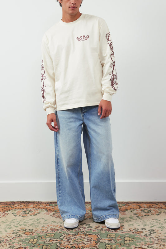 Person wearing a cream sweatshirt with floral patterns and light blue jeans on a plain background