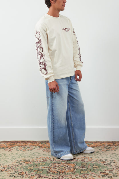 Person wearing a cream sweatshirt with red designs and light blue jeans on a white background