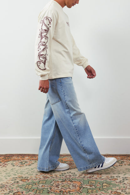 Person wearing a cream sweatshirt with intricate designs and blue jeans, walking on a patterned rug.