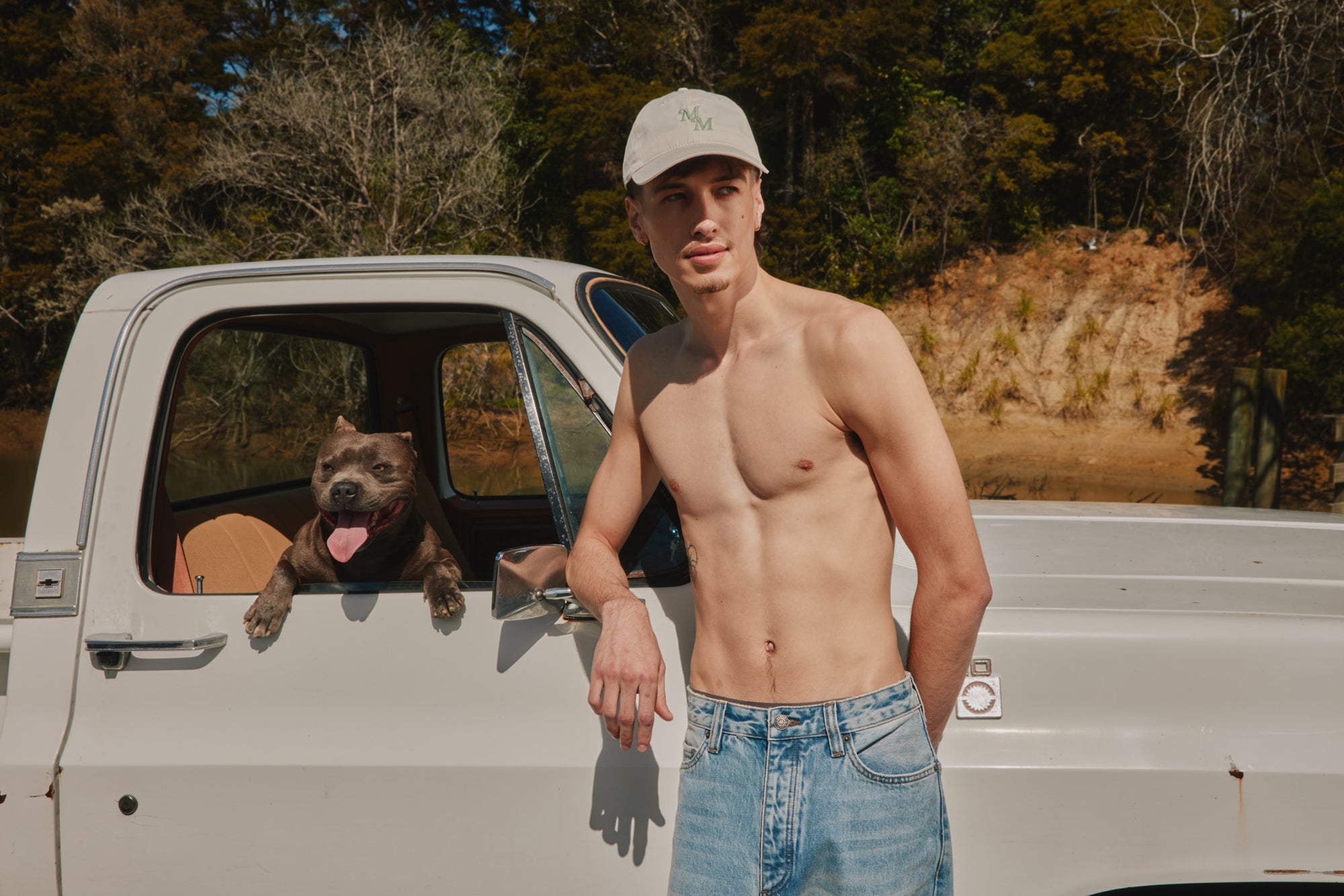 Man standing next to a truck with a dog in the back, outdoors.