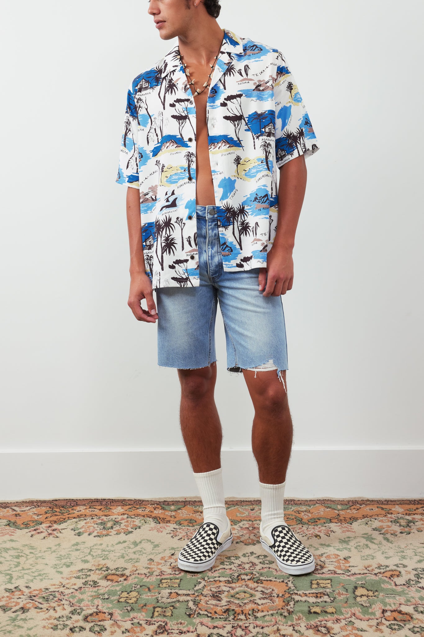 Person wearing a colorful patterned shirt and denim shorts on a plain background