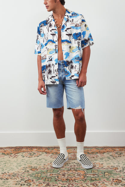 Person wearing a colorful patterned shirt and denim shorts on a plain background