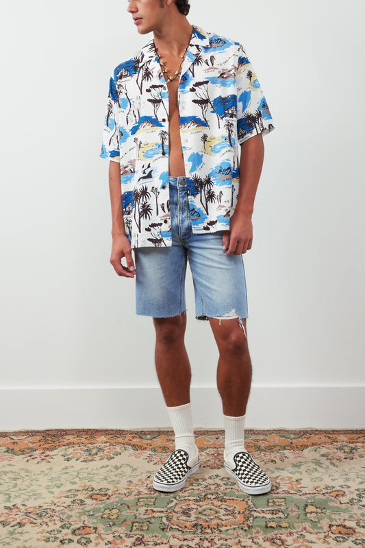 Person wearing a colorful patterned shirt and denim shorts on a plain background