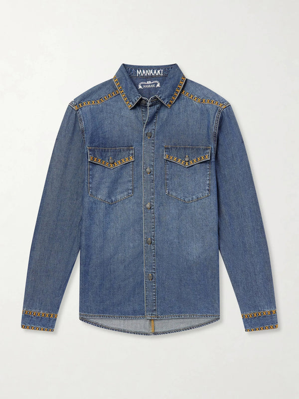 A blue denim long-sleeve button-up shirt by Manwaki, featuring decorative gold-colored embroidery along the collar, chest pockets, and cuffs, displayed flat against a light gray background.